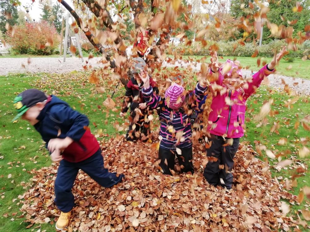 Neljä lasta heittävät syksyn lehtiä ilmaan ja nauravat