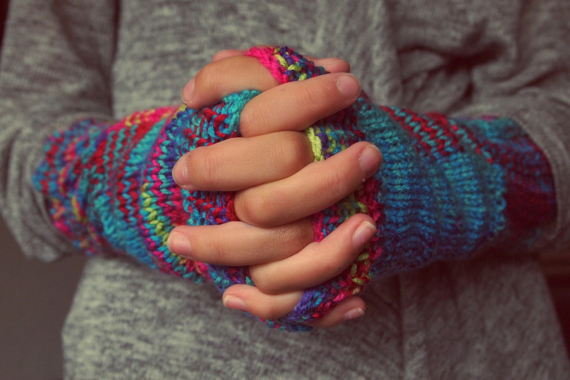 Kuvassa kädet ristissä, käsissä värikkäät käsineet